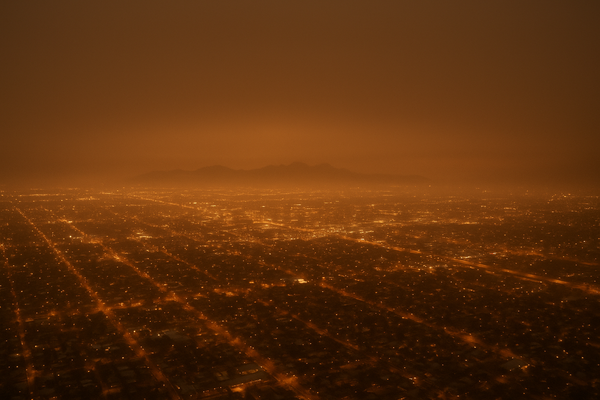 Wide aerial view of a hazy Phoenix valley at night, city grid lights diffused through smoggy air, no people or text visible