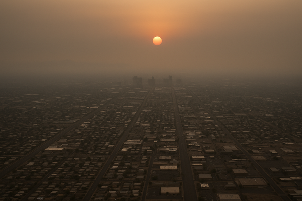 of a hazy desert sky over a flat urban grid at dusk, orange sun diffused through smog, no people