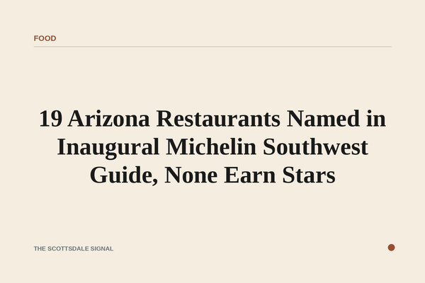 of a red Michelin Guide book resting on a bare wooden table, desert light through a window, no text visible