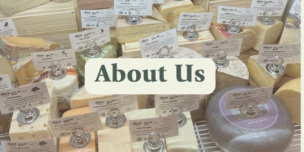 of a wooden cheese board with several wedges of artisan cheese, crackers, and a small jar of honey on a white marble surface