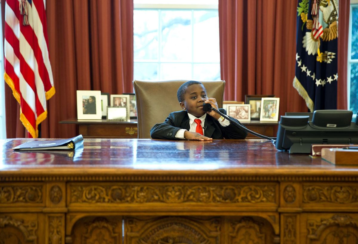 A kid takes a call at the Resolute Desk in the Oval Office. 