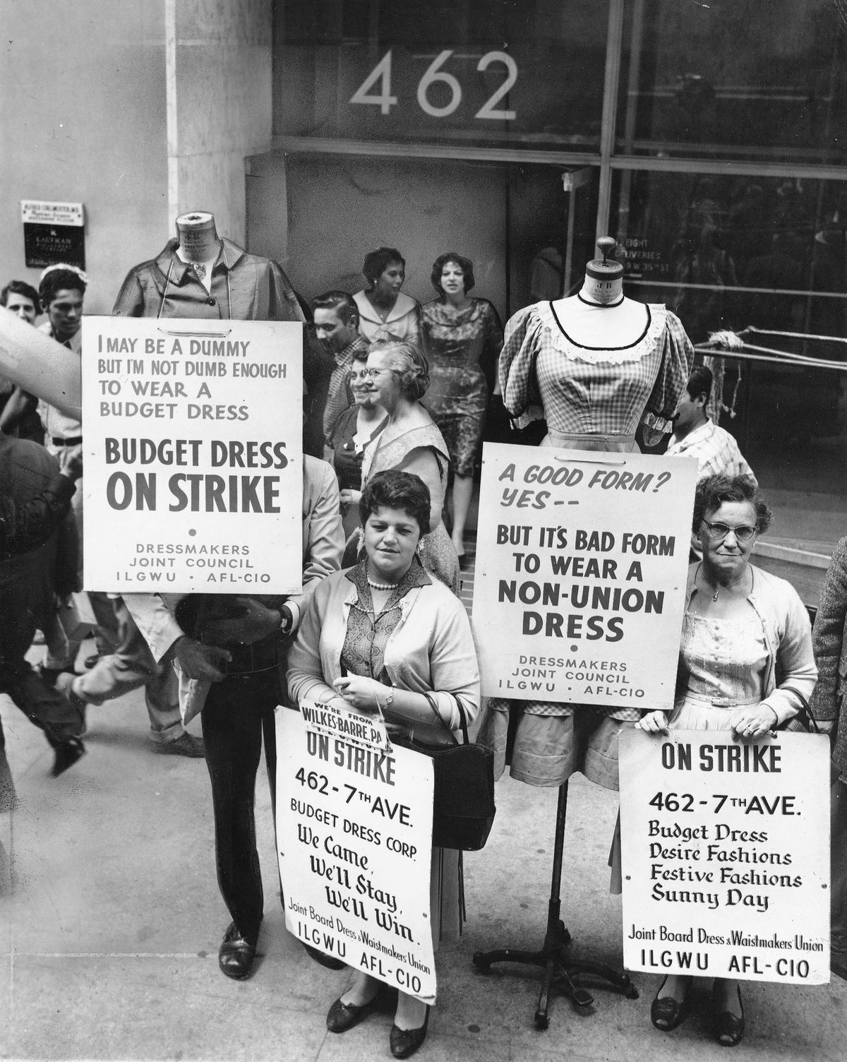 Black and white photo of women holding signs protesting Budget Dress. 