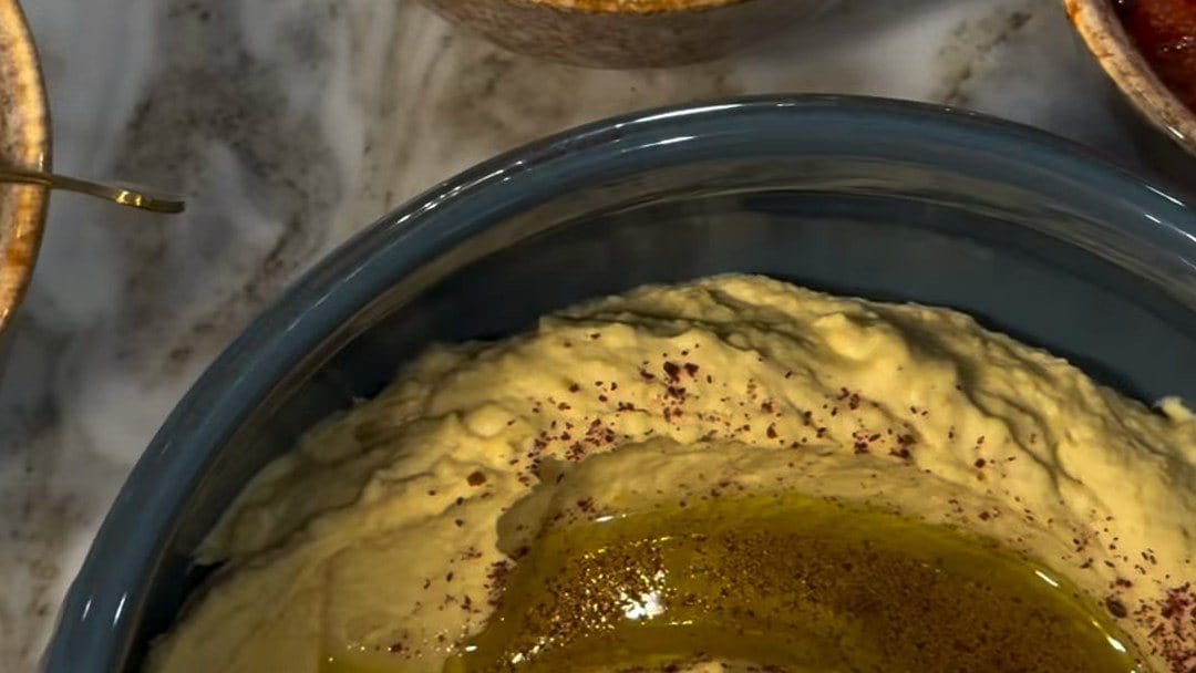 Creamy tahini and chickpea dip swirled with olive oil and dusted with sumac in a blue bowl