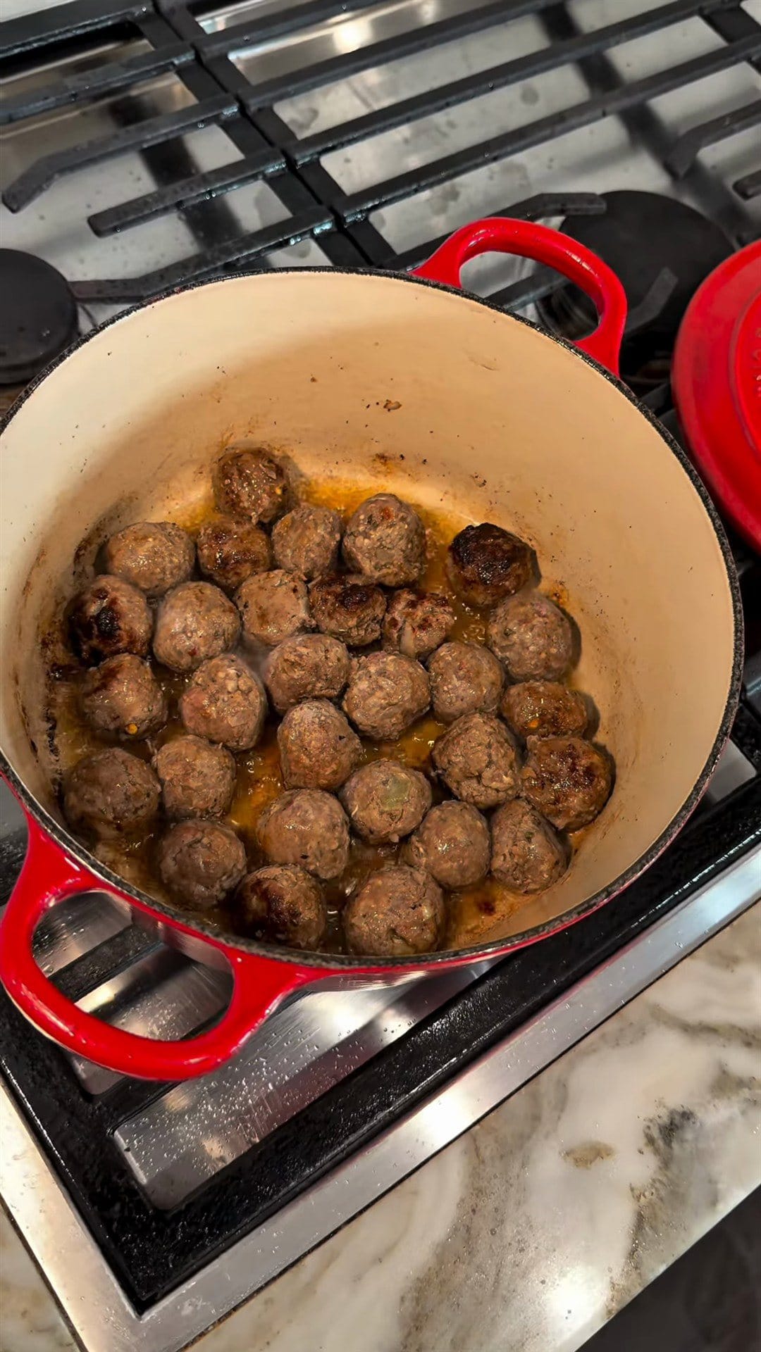 Golden-brown meatballs searing in a red Dutch oven on a gas stove