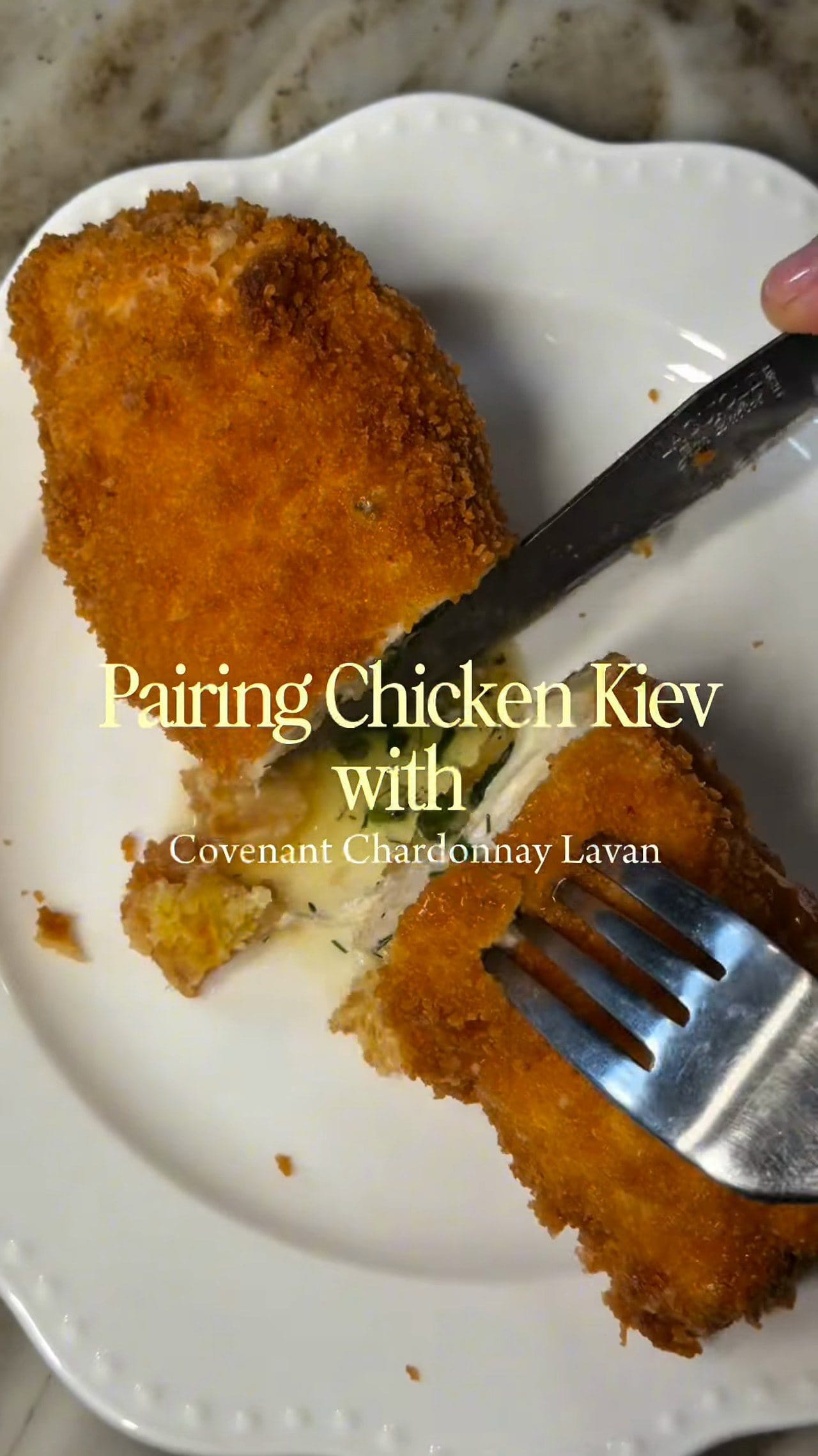 Chicken Kyiv cut in half on a white plate with a knife and fork, garlic butter and herbs spilling from the center