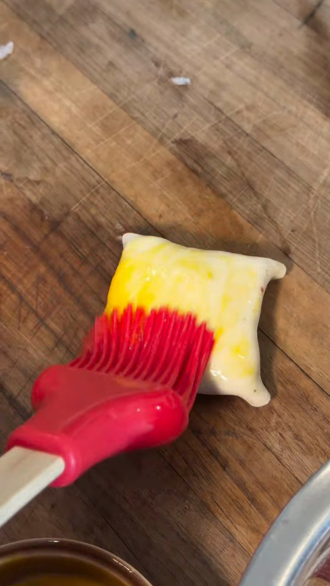 A red pastry brush painting egg wash over an unbaked samsa on a wooden board