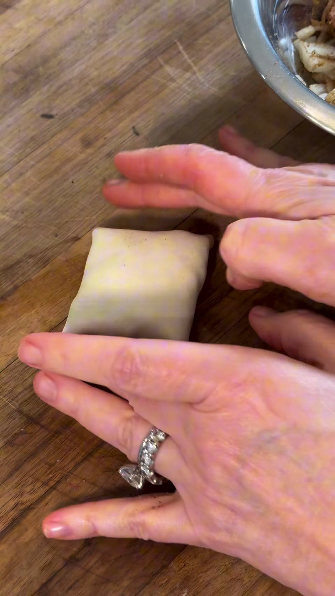 Hands folding a square of puff pastry into a closed parcel around the spiced beef filling on a wooden board