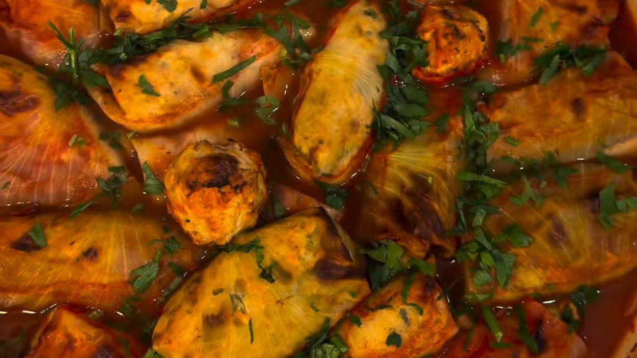 Close-up of browned stuffed cabbage rolls in tomato sauce, scattered with chopped fresh herbs