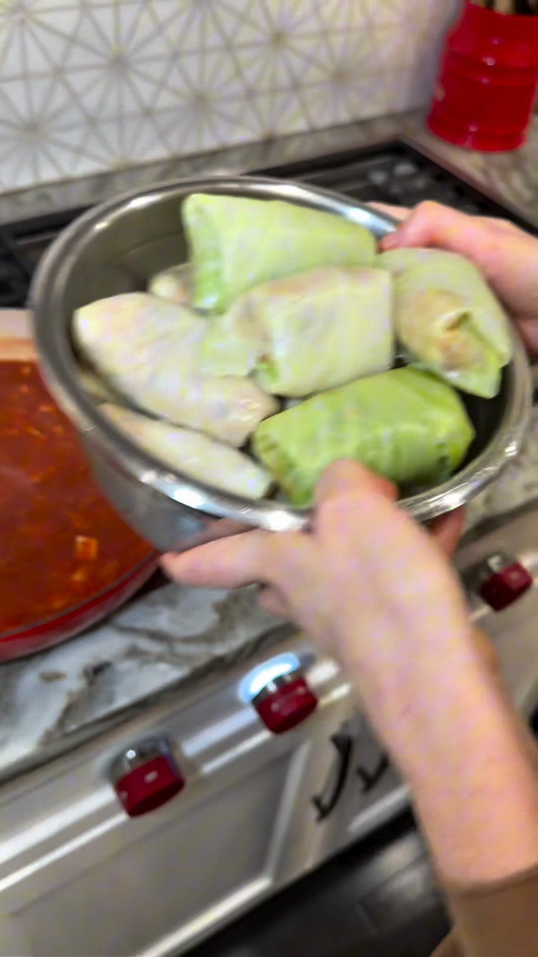 A steel bowl of rolled cabbage rolls, pale green leaves wrapped tight, carried to the stove