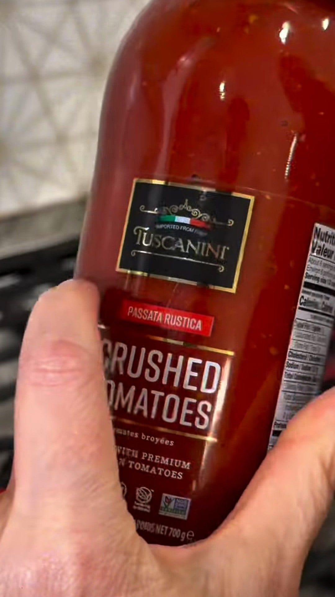 Close-up of a bottle of Tuscanini Passata Rustica crushed tomatoes in Anne's hand