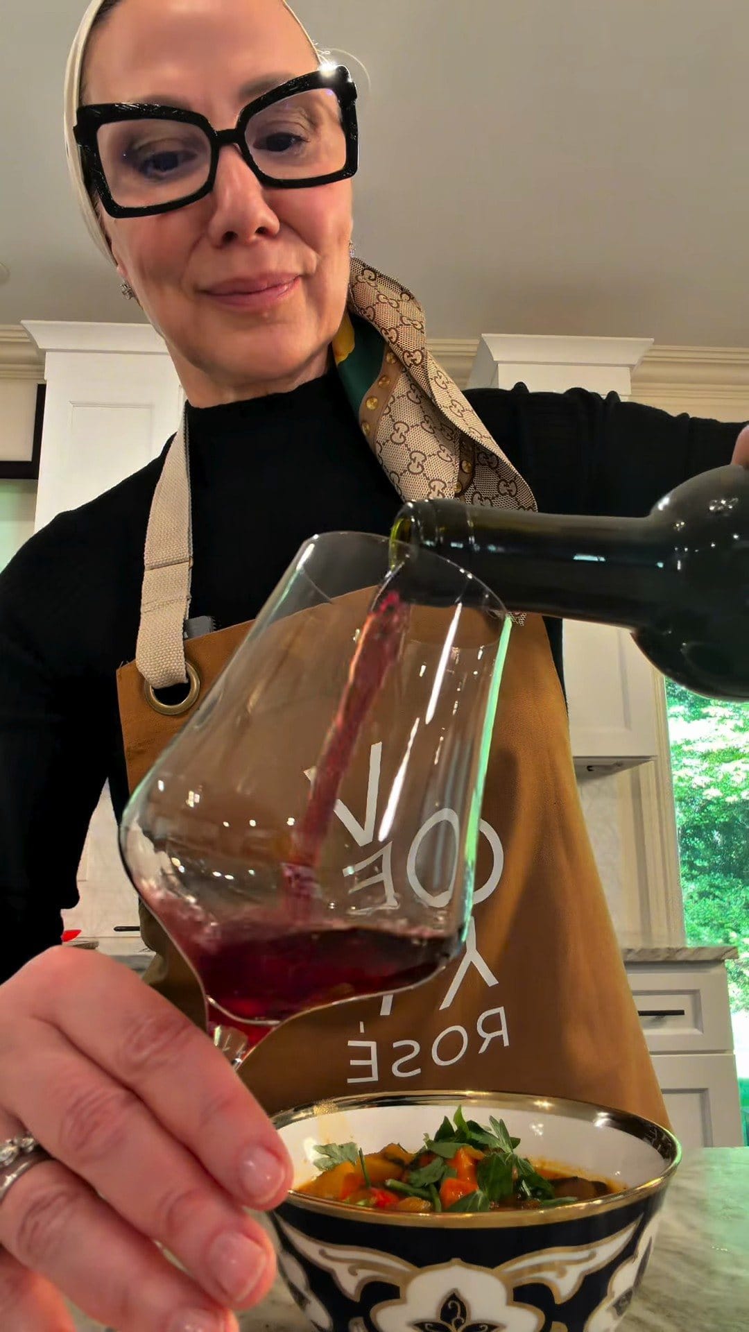 Anne pouring Hajdu Grenache into a large wine glass over a blue-and-white bowl of lagman topped with parsley