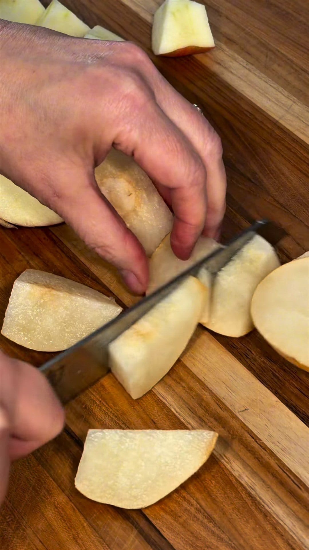 Anne's hands slicing a pear into chunks on a wooden cutting board, apple pieces beside it