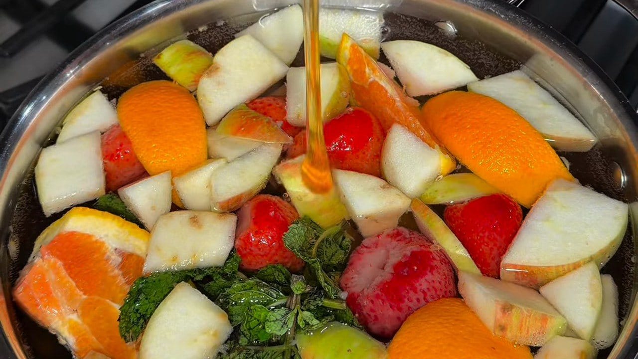 Chunks of apple and pear, orange wedges, strawberries and fresh mint in a pot of water as honey streams in