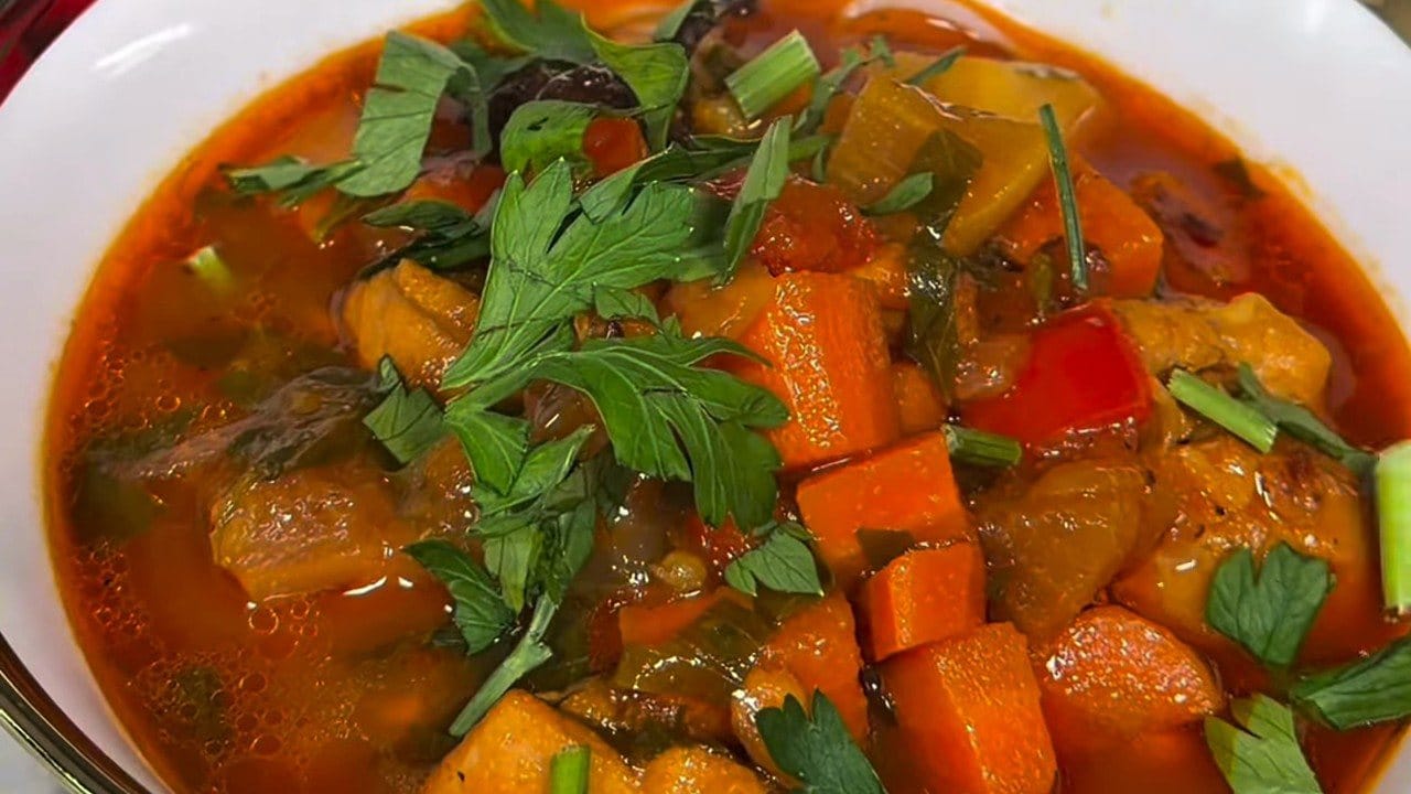 Close-up of lagman: chicken, carrots, red pepper and potatoes in a red tomato broth, topped with fresh parsley