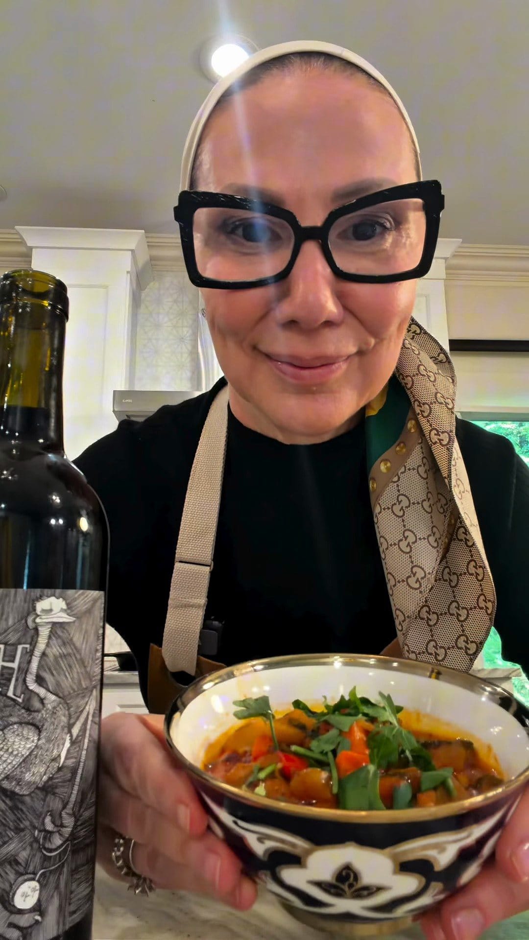 Anne smiling behind a blue-and-white Uzbek-style bowl of lagman topped with parsley, a bottle of Hajdu Grenache beside her