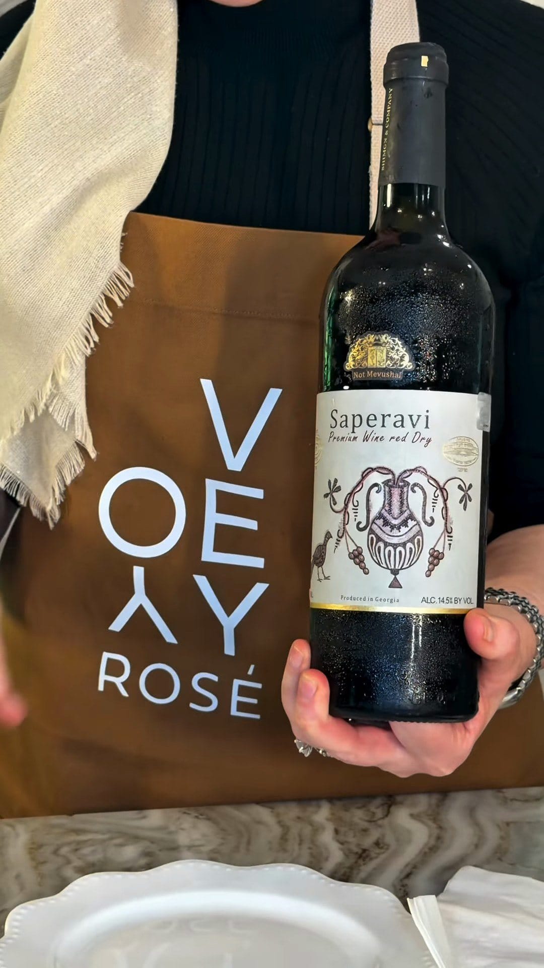 Anne holding a bottle of Saperavi, Premium Wine red Dry, with a clay amphora drawing on the label and a Not Mevushal seal on the neck