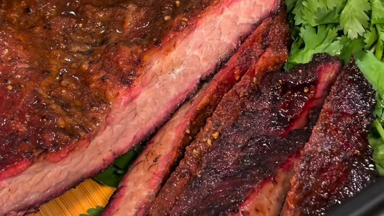 Close-up of sliced smoked brisket with a deep pink smoke ring and dark peppery bark, next to fresh cilantro