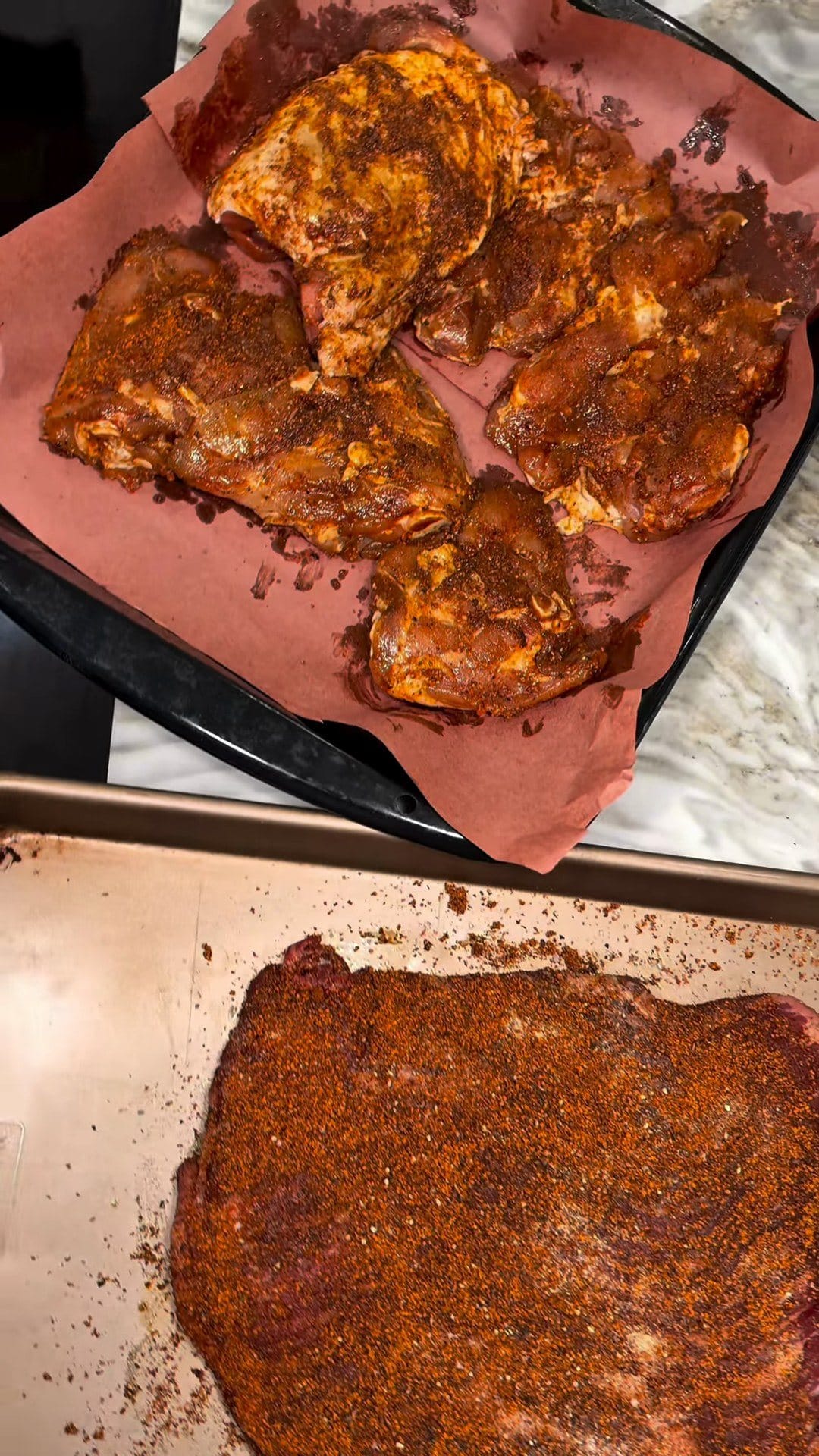 Bone-in chicken thighs on butcher paper and a brisket on a sheet pan, both coated in a red smoky rub
