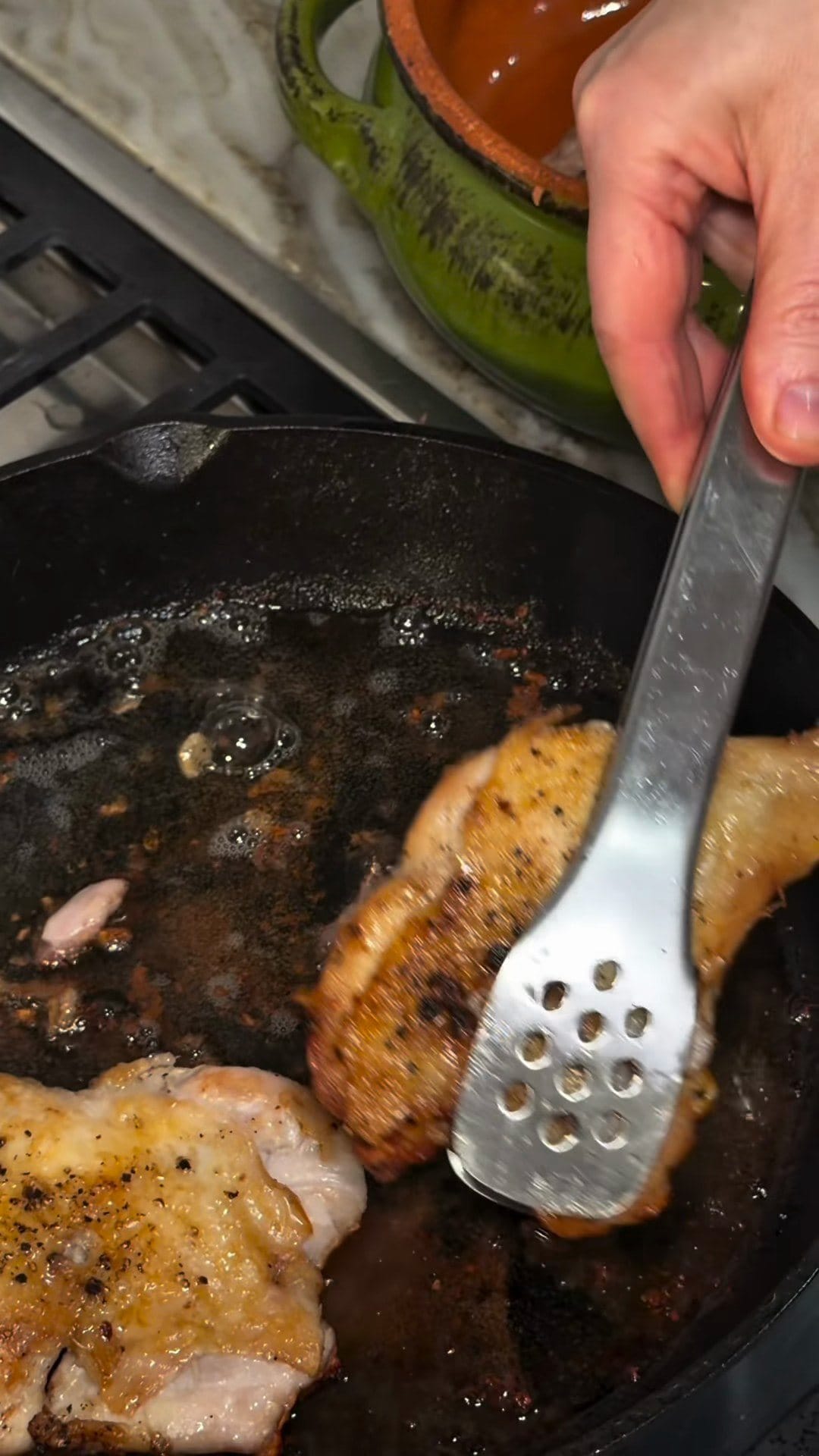 A slotted spatula flipping a golden, crispy chicken thigh in a cast-iron skillet