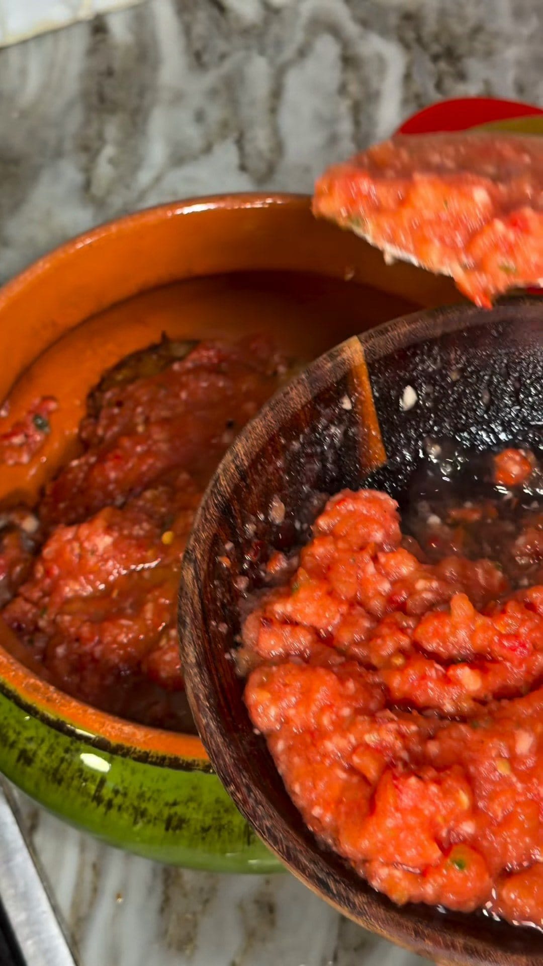 Chunky fresh tomato sauce spooned from a wooden bowl over chicken in a terracotta dish