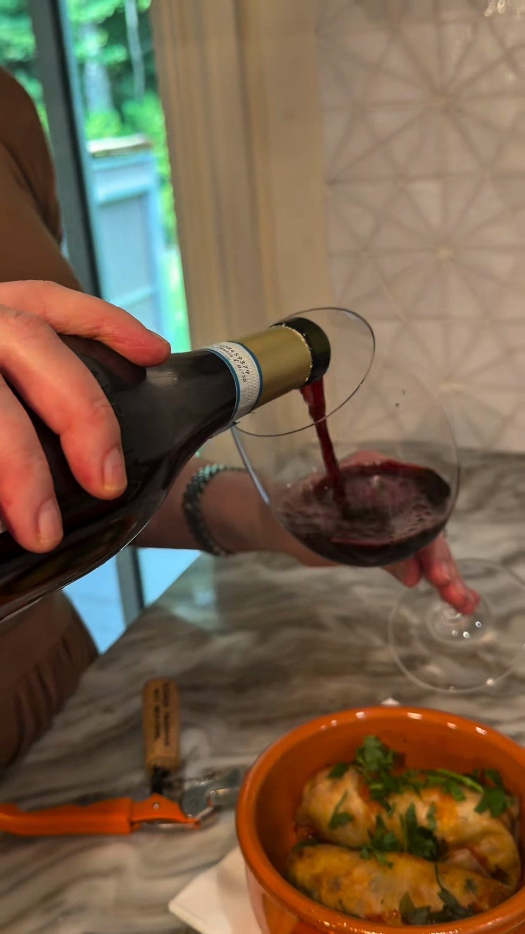 Barbera being poured into a large red-wine glass, with a terracotta bowl of herb-topped stuffed cabbage rolls in front