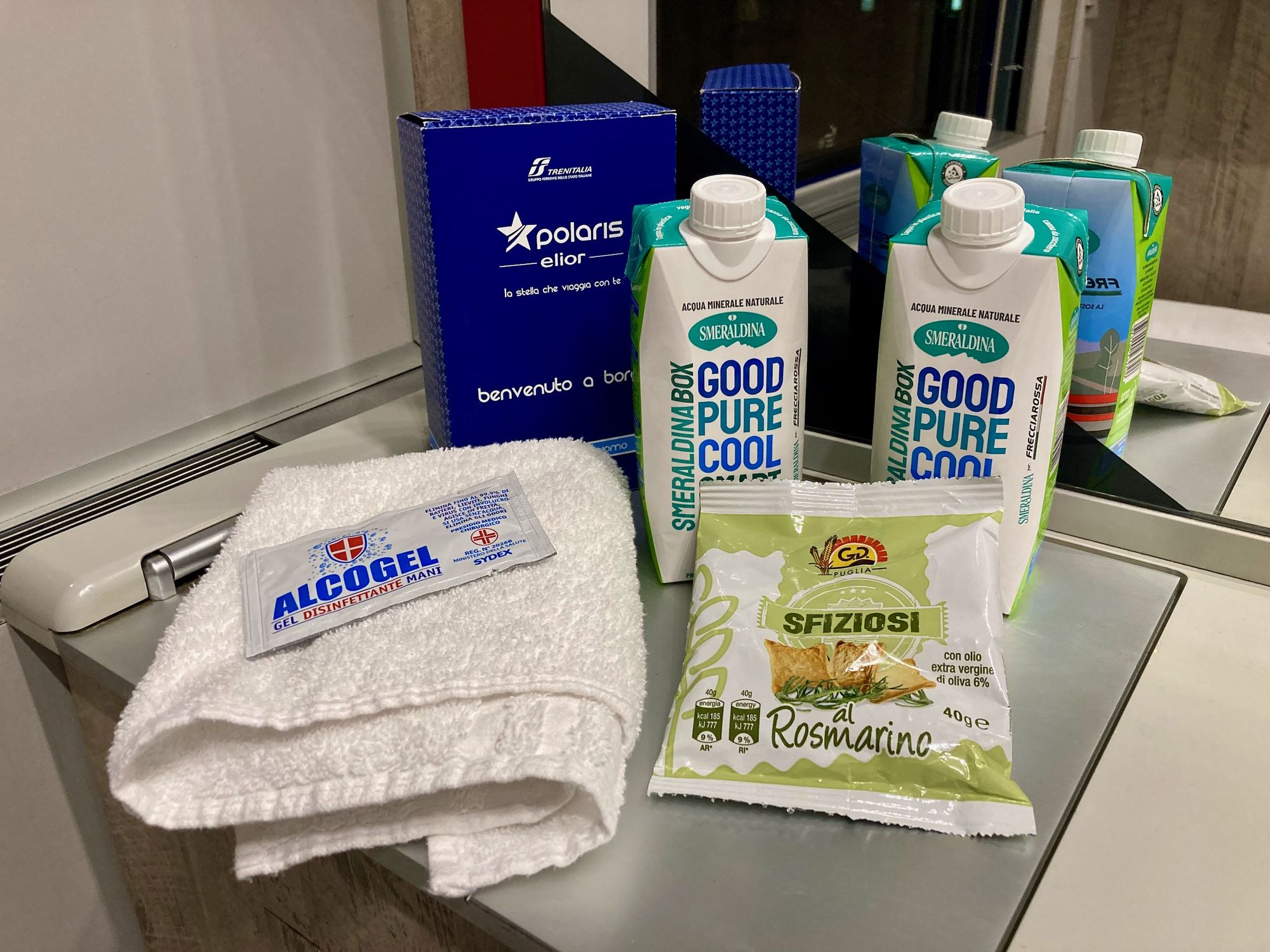 Handtuch, Desinfektionsgel, zwei Päckchen Wasser, ein Reiseset und eine Tüte Rosmaringebäck