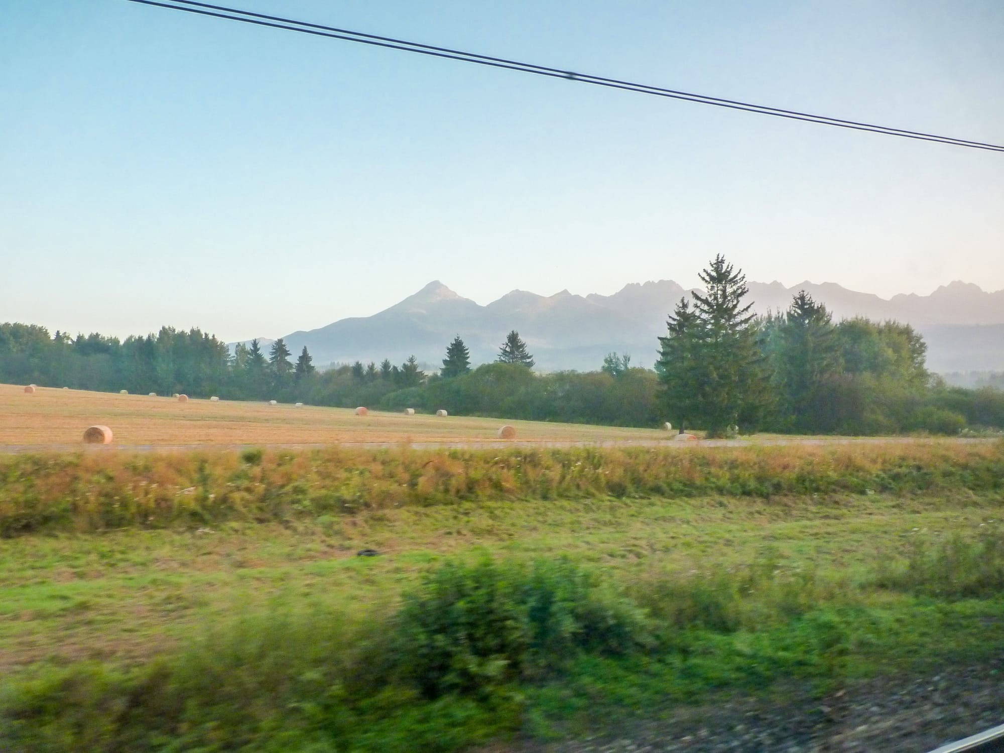 Fotos aus dem Zug, im Vordergrund Wiesen, im Hintergrund hohe Berge