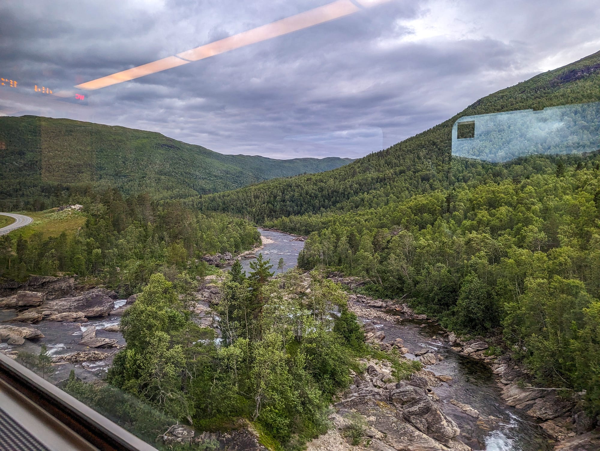 Blick auf dem Zugfenster auf einen reißenden Fluss auf der Nordlandbahn