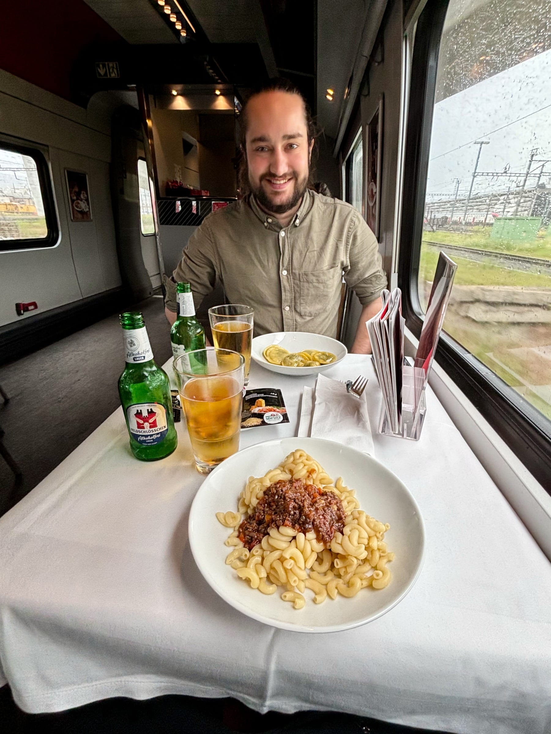 Eine Person sitzt am Tisch mit zwei Tellern mit Pastagerichten und Getränken