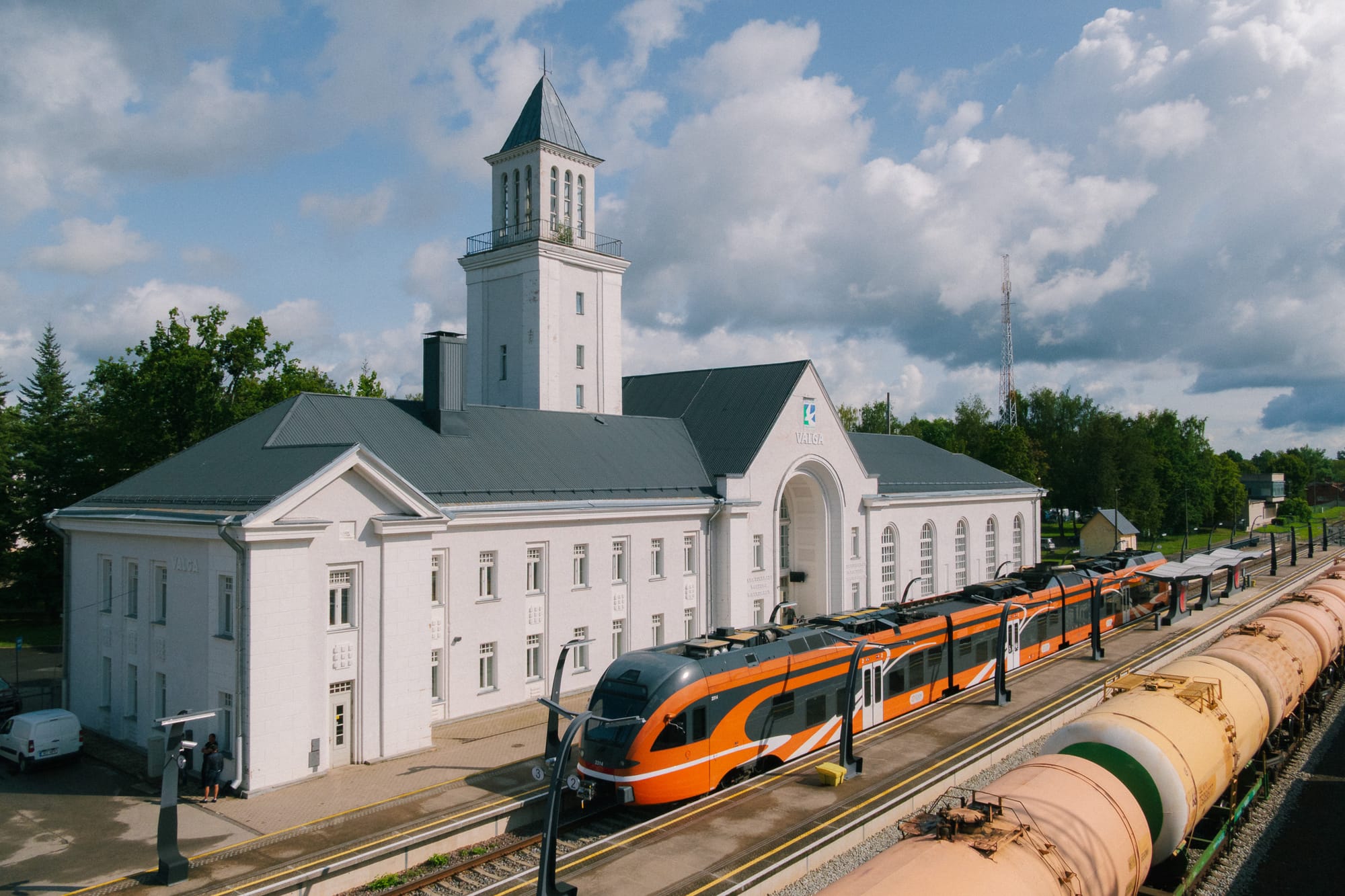Oranger Dieseltriebwagen vor weißem Bahnhofsgebäude