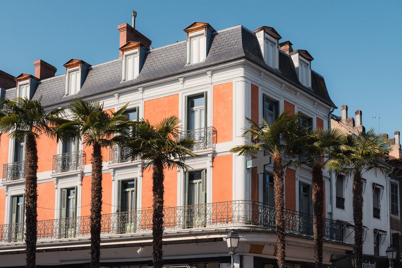 Palmen vor pastellfarbenen Fassaden und schmiedeeisernen Balkonen in Tarbes