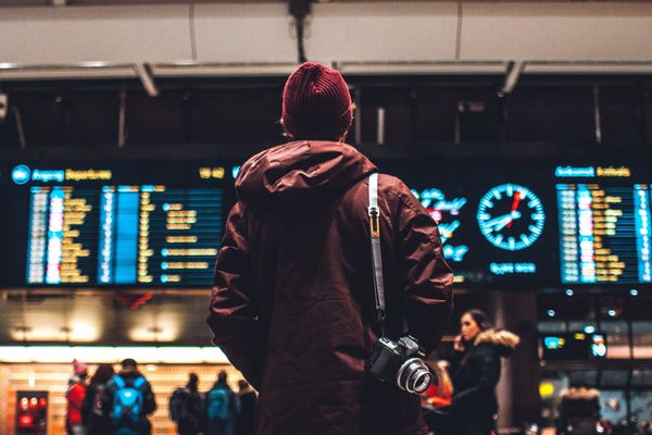 Person mit Kamera vor einer Abfahrtstafel am Bahnhof