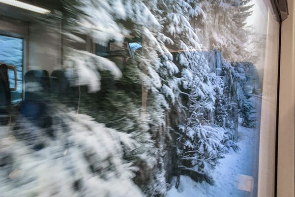 Blick aus dem Zugfenster auf eine Felswand mit Schnee