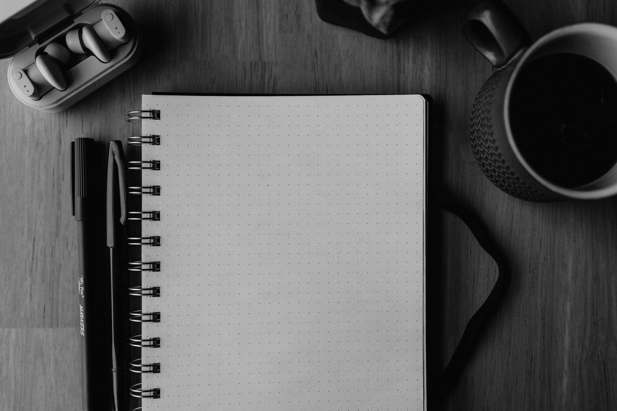 Notebook, pen, headphones, and coffee on a wooden desk.
