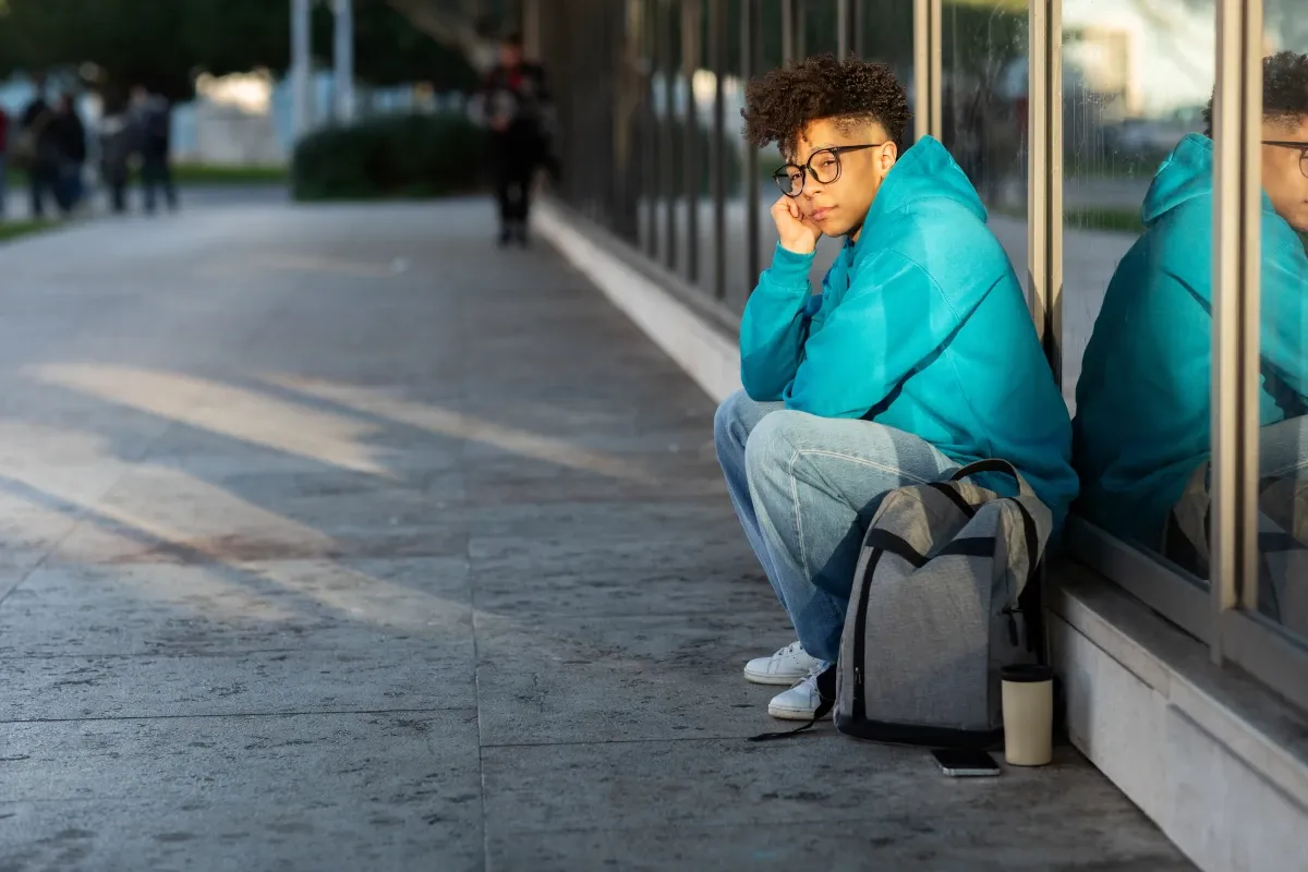 A student sitting alone with a backpack outside a campus building