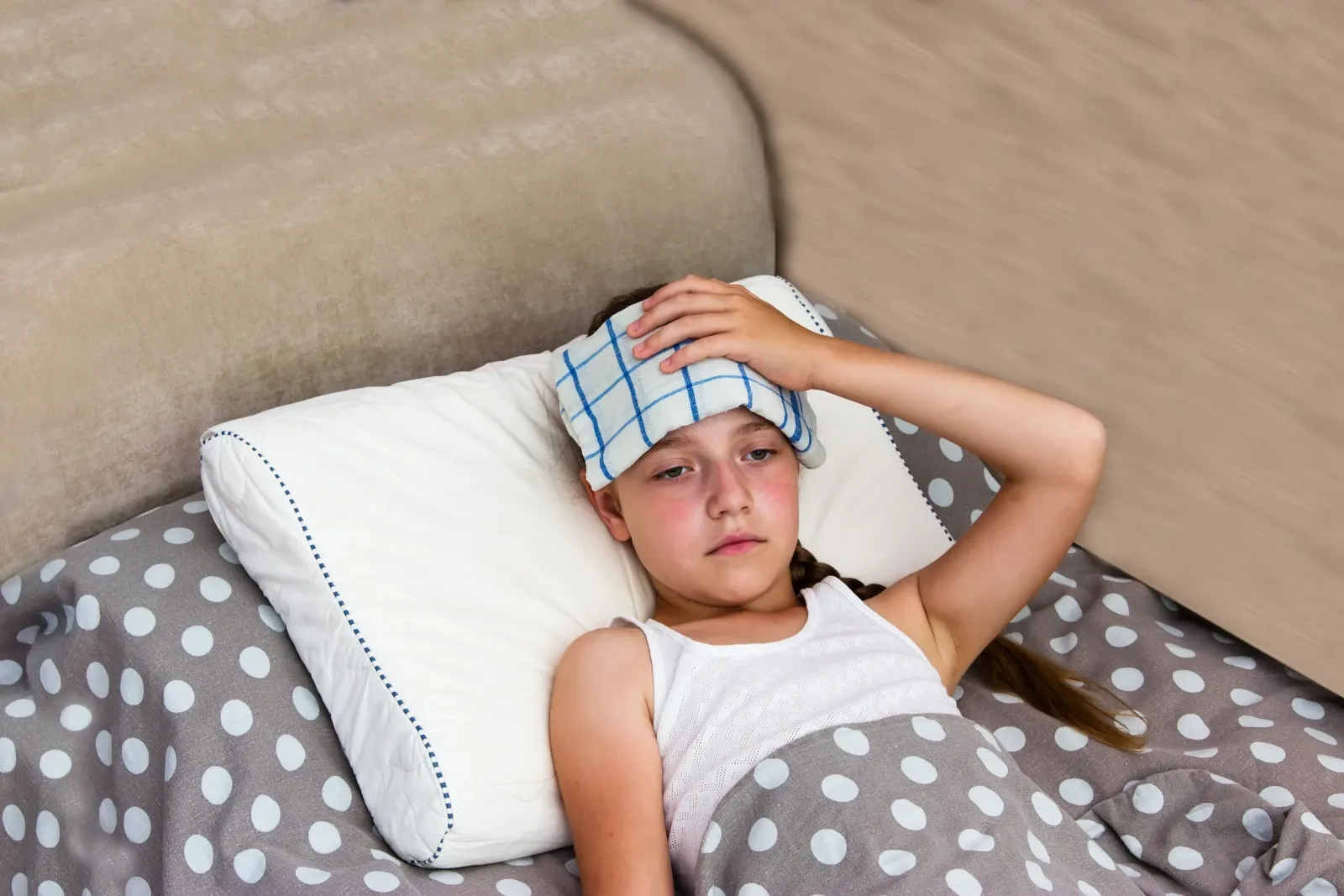 Child lying in bed with a cool cloth on their forehead while recovering from heat illness