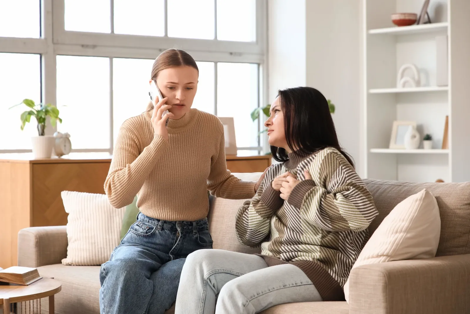 Person calling for emergency help while supporting someone with possible heart attack symptoms at home.