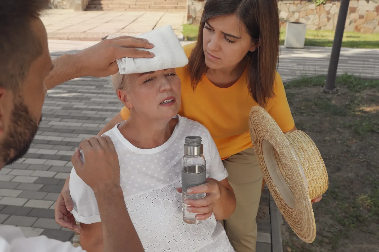 People helping an older woman showing signs of heat exhaustion by cooling her with water and a damp cloth