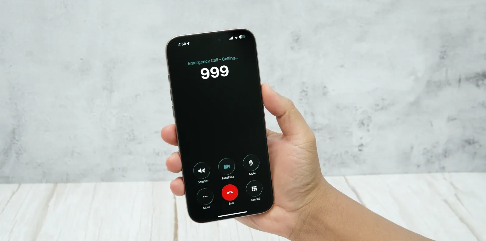 Hand holding a smartphone during a 999 emergency call.