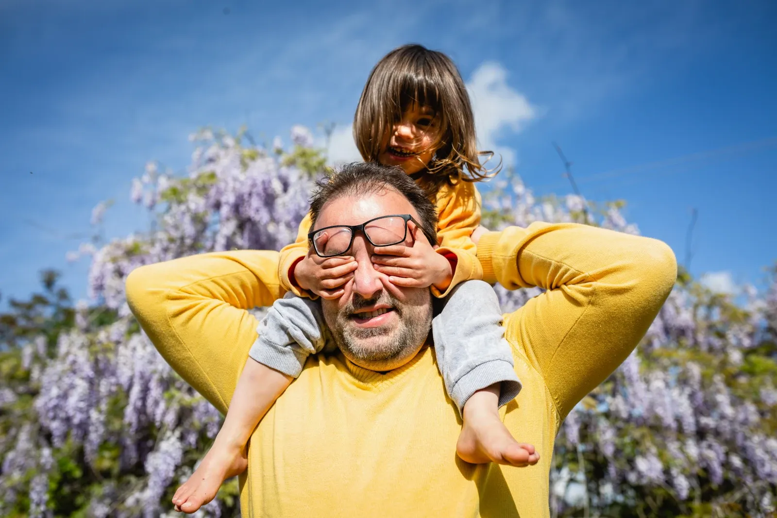 A father carrying a young child on his shoulders while playing outdoors.