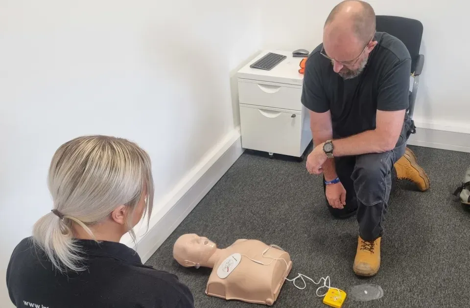 Employee practising CPR and AED use on a manikin during a workplace first aid course.