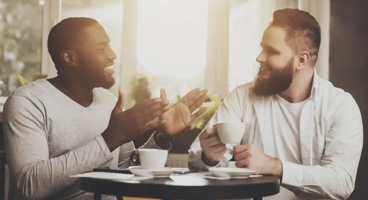 Two men having a relaxed conversation over coffee, representing supportive discussions about mental health.