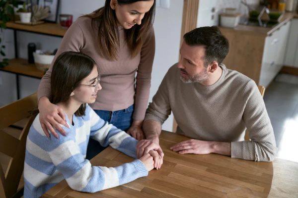 Parents talking with their teenage daughter at a kitchen table.