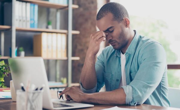 Office worker holding his head while looking at a laptop, illustrating workplace stress and workload pressure.
