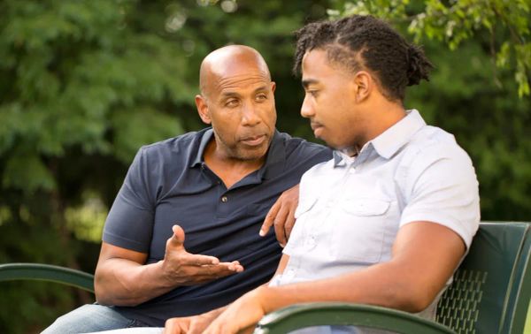 An older man speaking supportively with a younger man during a serious outdoor conversation