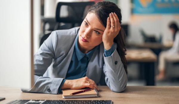 Office worker leaning on one hand at her desk, looking stressed in a workplace setting