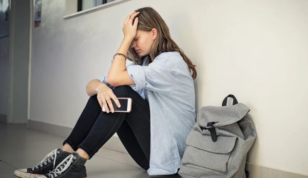 Teenage student sitting on the floor with a severe headache beside a backpack