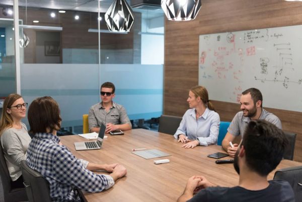 A workplace team meeting in a boardroom, with colleagues discussing plans around a table