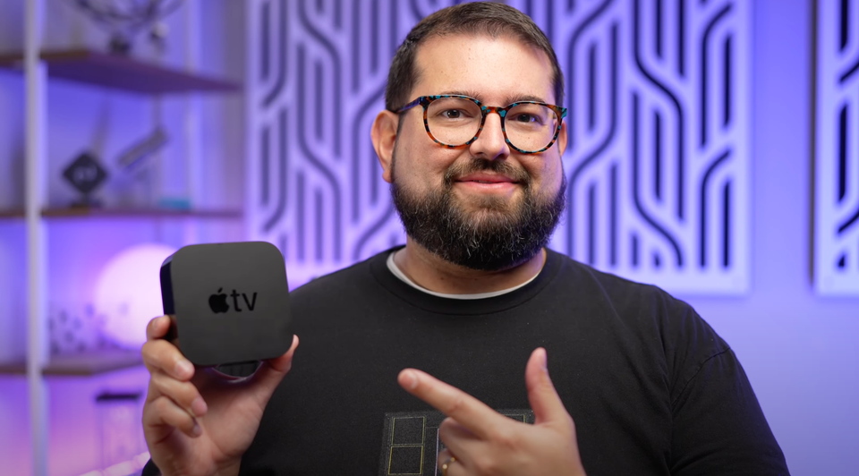 Stephen Robles holding an Apple TV hardware box and pointing at it.