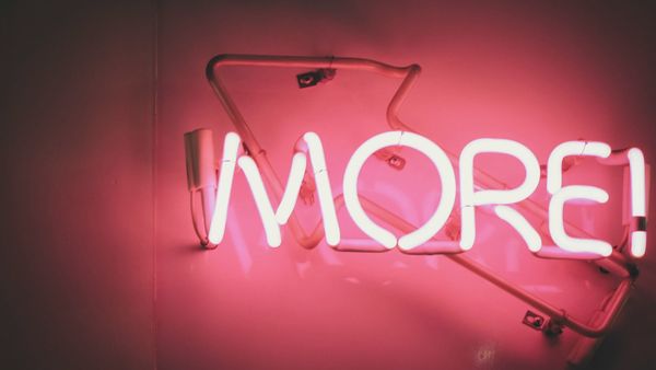 the word more in bright pink neon tube lighting against a darker pink wall